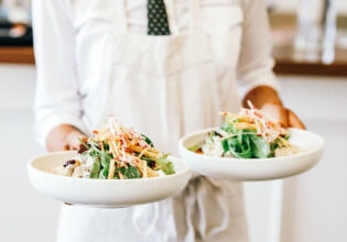 a person in white holding two plates of food at Plantation Cafe, Bowral
