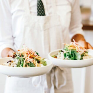 a person in white holding two plates of food at Plantation Cafe, Bowral