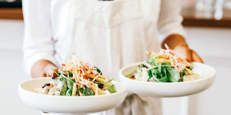a person in white holding two plates of food at Plantation Cafe, Bowral