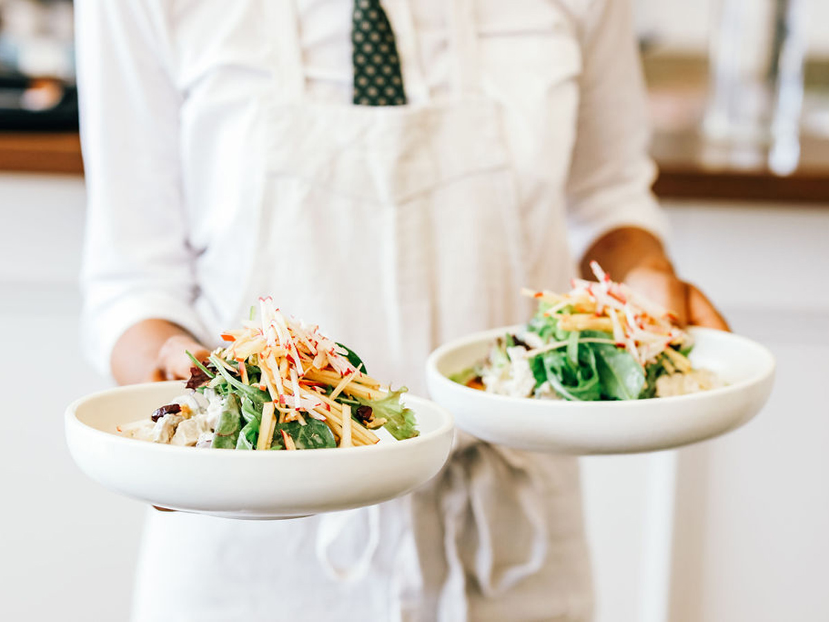 a person in white holding two plates of food at Plantation Cafe, Bowral