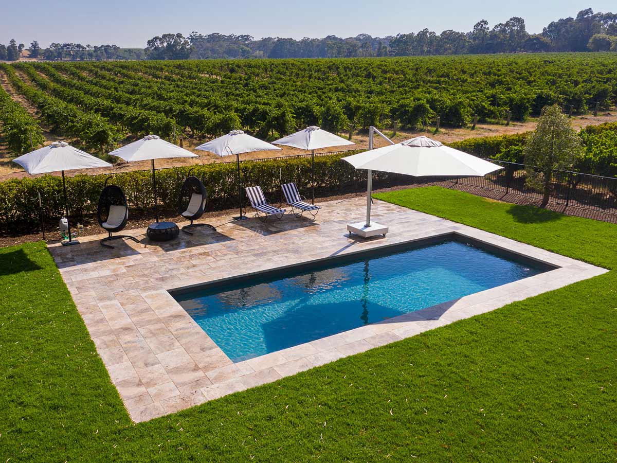 an outdoor pool with umbrellas and sun loungers surrounded by an expansive vineyard in Le Mas, Barossa Valley