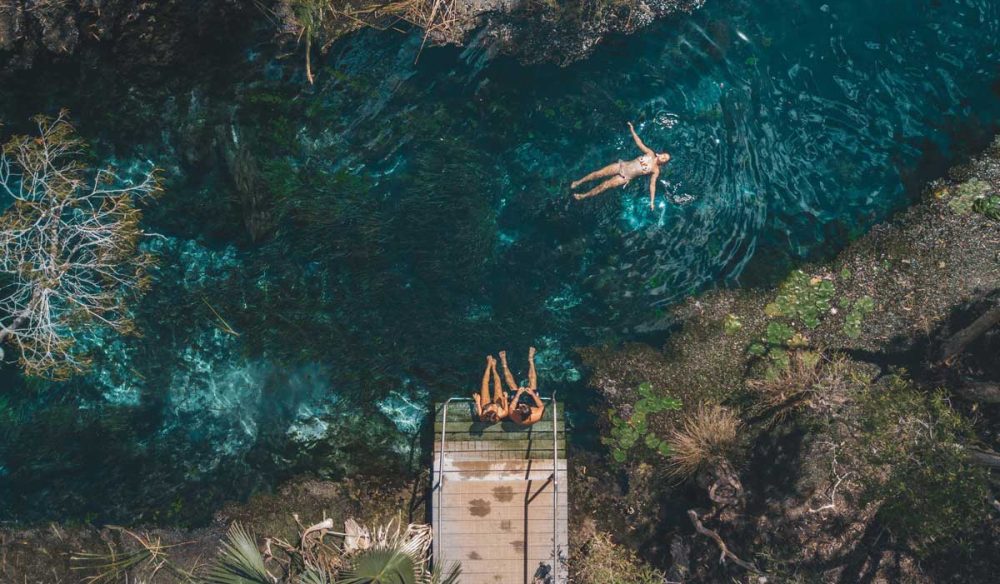 an aerial shot of a girl floating and two girls sitting on the edge of Mataranka Thermal Pool