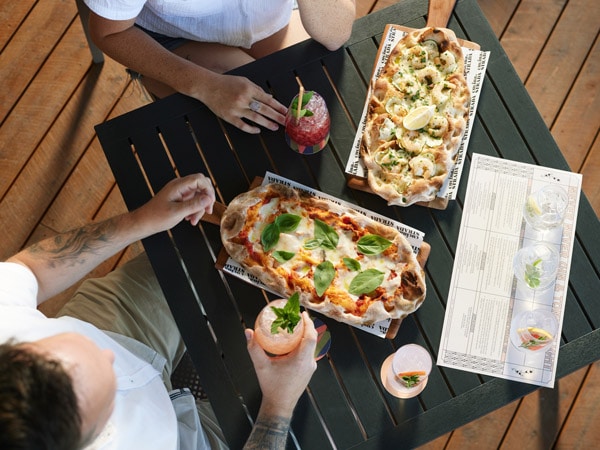 two people sharing salami pinsa and drinks on the table at Never Never Distilling Co.