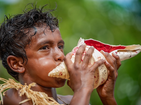 seorang anak laki-laki meniup cangkang keong