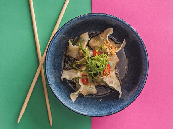 Bowl of barramundi in black vinegar with herbs and chopsticks on the side