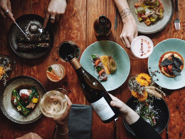 a table top view of meals with a hand holding a bottle of wine