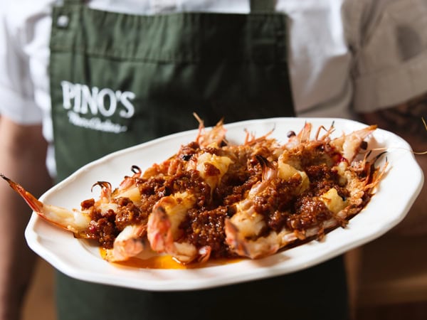 a chef holding a plate of cooked shrimp at Pino’s Vino e Cucina al Mare