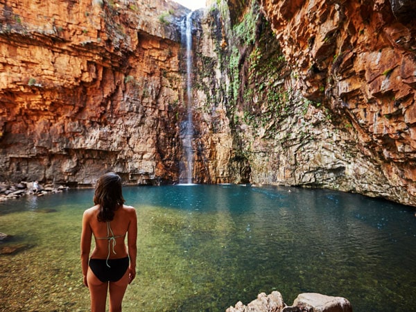seorang wanita berdiri di depan air terjun Emma Gorge