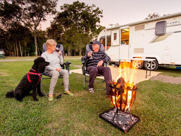 an old couple sitting by the bonfire and sipping wine next to their camper van