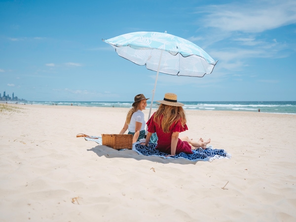 two women sitting under a beach umbrella