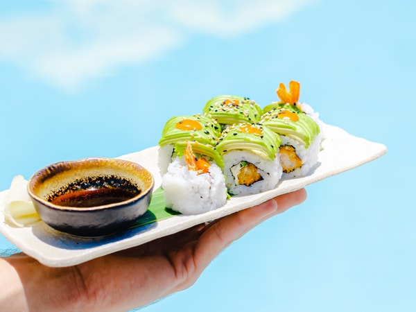 a hand holding a plate of california maki rolls at Cali Beach Club