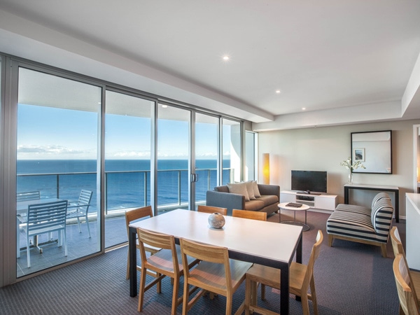 a dining area facing the glass windows and balcony overlooking the beach at Hilton Surfers Paradise Hotel & Residences