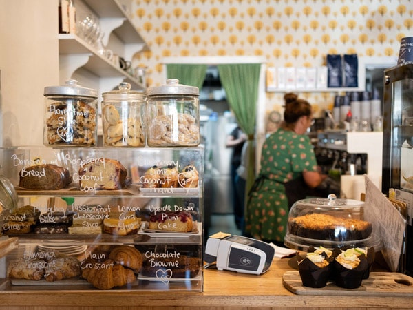 Cakes and sweet treats in cabinet at Food Wine Friends in Bright with barista making coffee in background