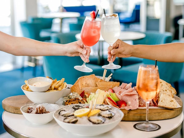 clinking cocktail glasses on top of a food spread at Nineteen at the Star, Broadbeach