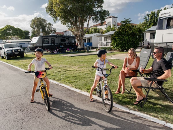 kids riding a bike with their parents sitting outside the caravan park at Nobby Beach Holiday Village
