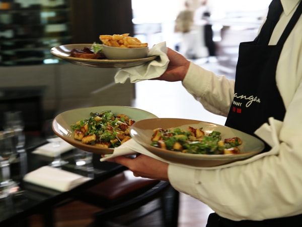 a waiter holding plates of food at Glass Brasserie