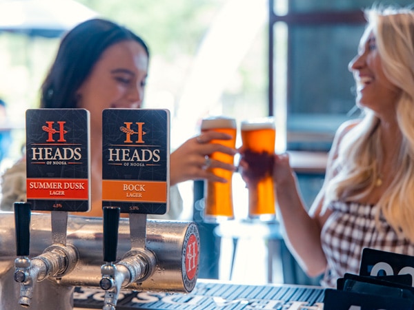 two women clanking beer glasses at Heads of Noosa