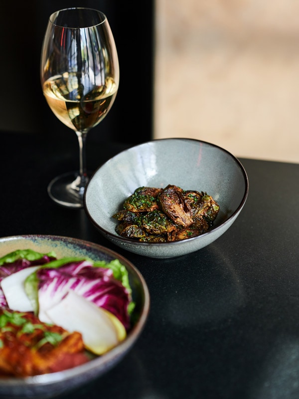 Brussel sprouts and vegetable dishes with glass of white wine at Lilotang in Canberra.