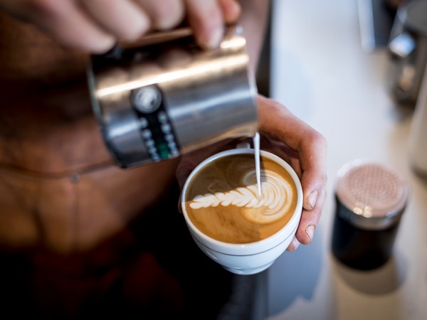 a hand pouring milk over coffee at Meccanico Espresso + Wine