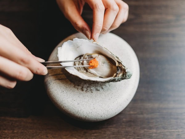 a hand decorating an oyster at Mu Omakase, Canberra