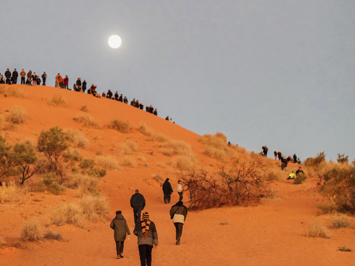 A group of people climbing a sand dune at the Birdsville Big Red Bash in Queensland's Simpson Desert