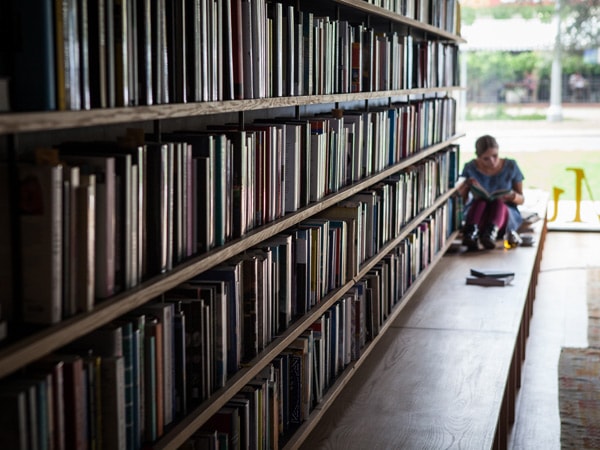 a woman reading a book at the further end of the small bookshelf in Muse, East Hotel Canberra