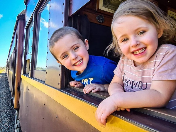two kids peeking from the train's window smiling, Kiama Picnic Train