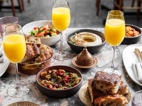 three glasses of mimosas alongside the food on the table at Meze & Mimosas Babylon