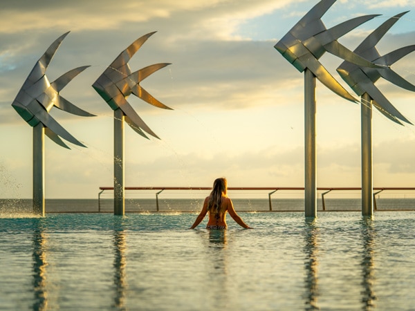 a young woman standing between sculptural fish at Cairns Esplanade Lagoon at sunrise