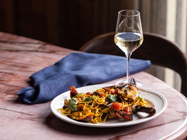 a plate of Marron Spaghetti alongside a champagne glass on the table at Lana, Sydney