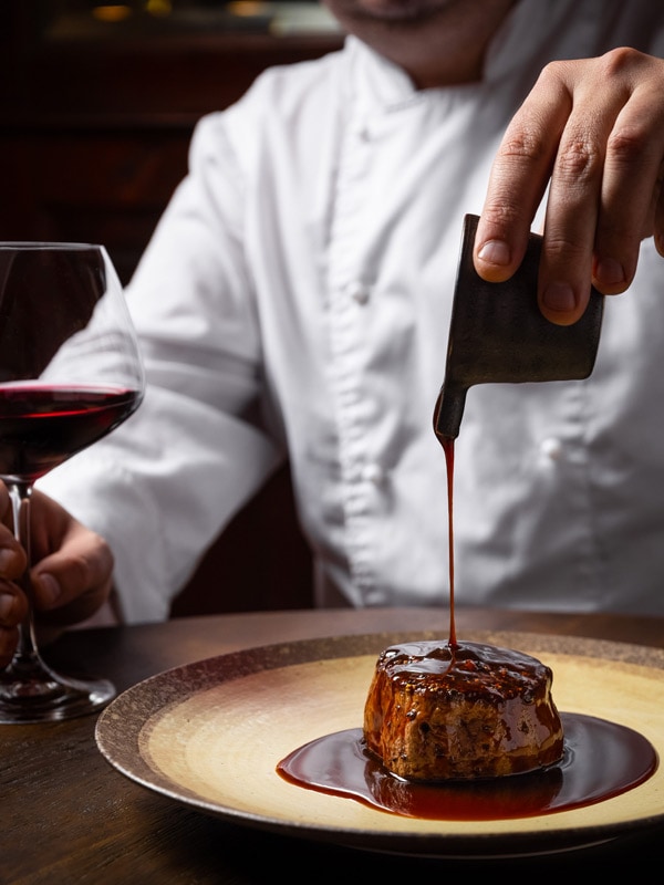 the head chef Damian Brabender pouring sauce over a meat dish at OTIS