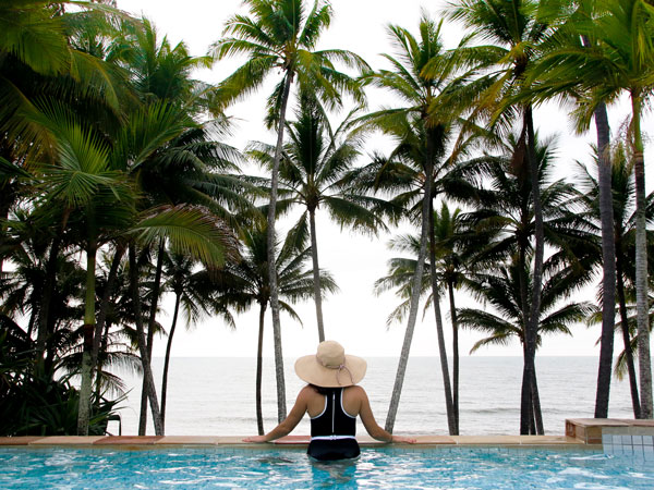 a woman relaxing at the infinity pool with a backdrop of palm trees at Alamanda Palm Cove by Lancemore