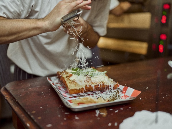 sprinkling pizza toppings at Franc Jrs, Coolangatta