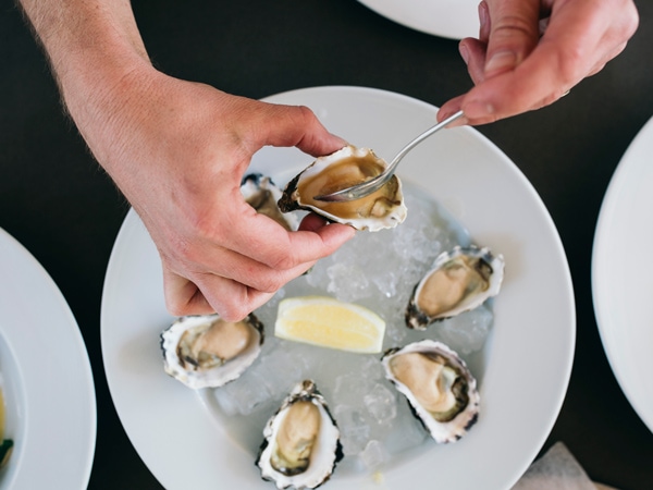 a hand getting oyster meat from the shell at Fins Restaurant & Bar