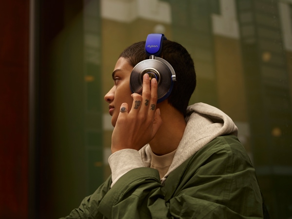 a person listening to music with one hand holding the left side of Dyson Zone noise-cancelling headphones