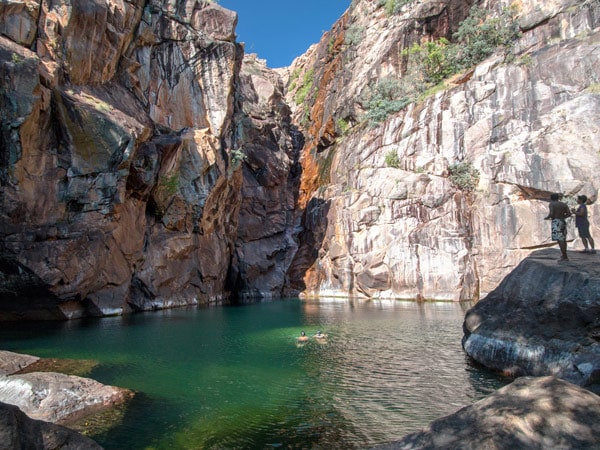 two people standing on the side of a rock formation at Motor Car Falls, Kakadu