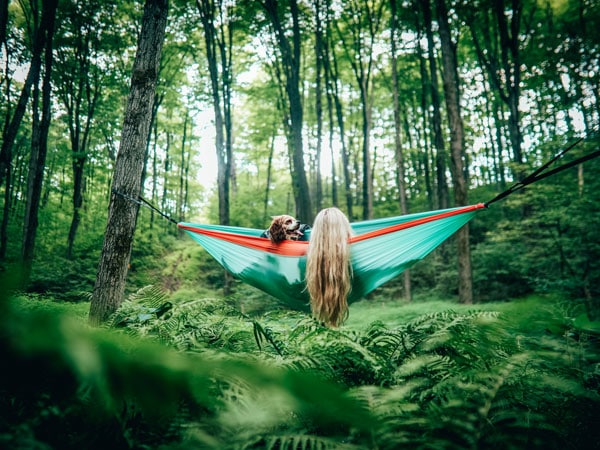 a woman with her dog lying on a Nakie Hammock in the forest