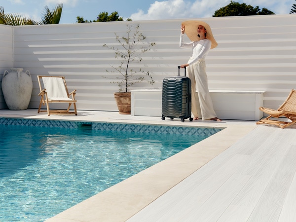 Lady in wide-brimmed hat with Samsonite Proxis suitcase by a pool in Byron Bay.