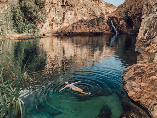 a woman floating on a pristine natural waterfall and plunge pool at the base of steep gorge walls in Maguk