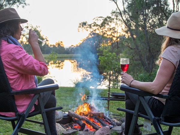 two people sitting by the bonfire and drinking wine 
