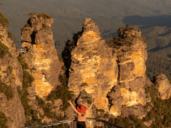 a woman posing with arms raised with Three Sisters in the background