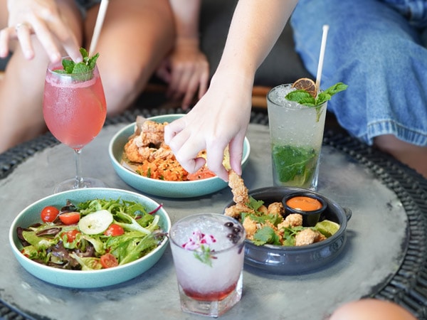 hand holding fried calamari with food and drinks on the table at The Dock, Mooloolaba