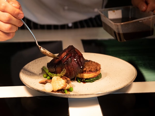 a hand holding a spoon while pouring sauce over a dish at Tali, Alice Springs