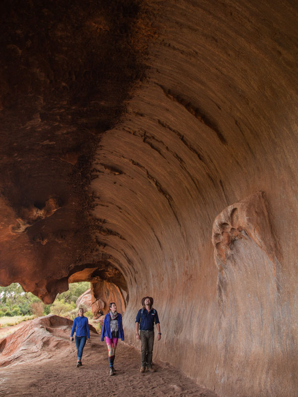 three people walking under a rock formation, Wayoutback Australian Safaris