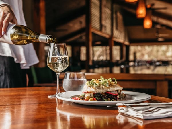 pouring wine into glass alongside a plate of food on the table