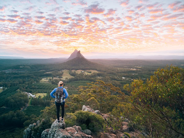 a hiker admiring the view atop Glass House Mountains