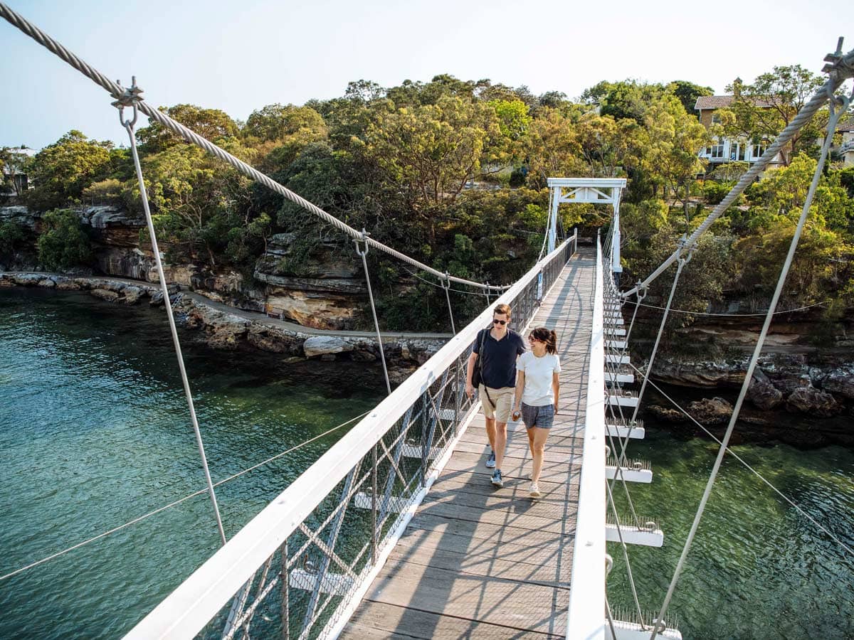 A couple cross the suspension bridge at Parsley Bay while walking the Bondi to Manly coastal walk