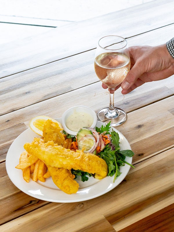 a hand holding a glass alongside a plate of food on the table