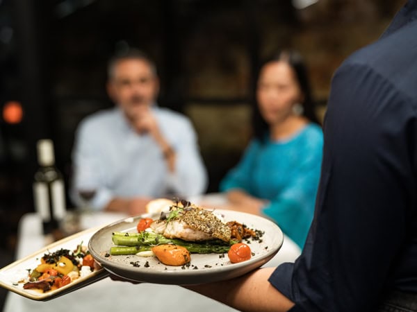 a close-up shot of a waiter serving a plate of food at Carmichael's Restaurant