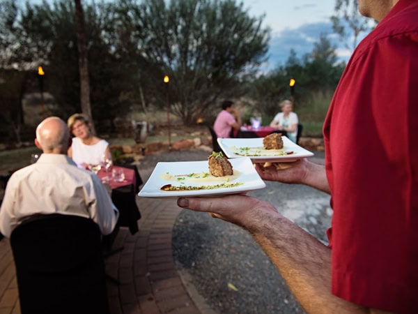 a waiter holding plates of food at the open-air Under a Desert Moon dinner at Discovery Resorts - Kings Canyon